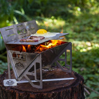 Portable stainless steel camp grill cooking bacon and eggs on a tree stump in the forest