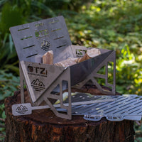 Portable stainless steel campfire stove with wood pieces, set on a tree stump in the forest.