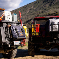 Two off-road vehicles with mounted gear bags and utility accessories in a mountain setting.