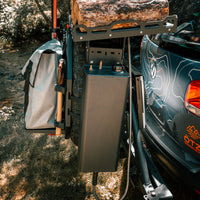 Rear-mounted camping storage and gear system attached to SUV with firewood and equipment.