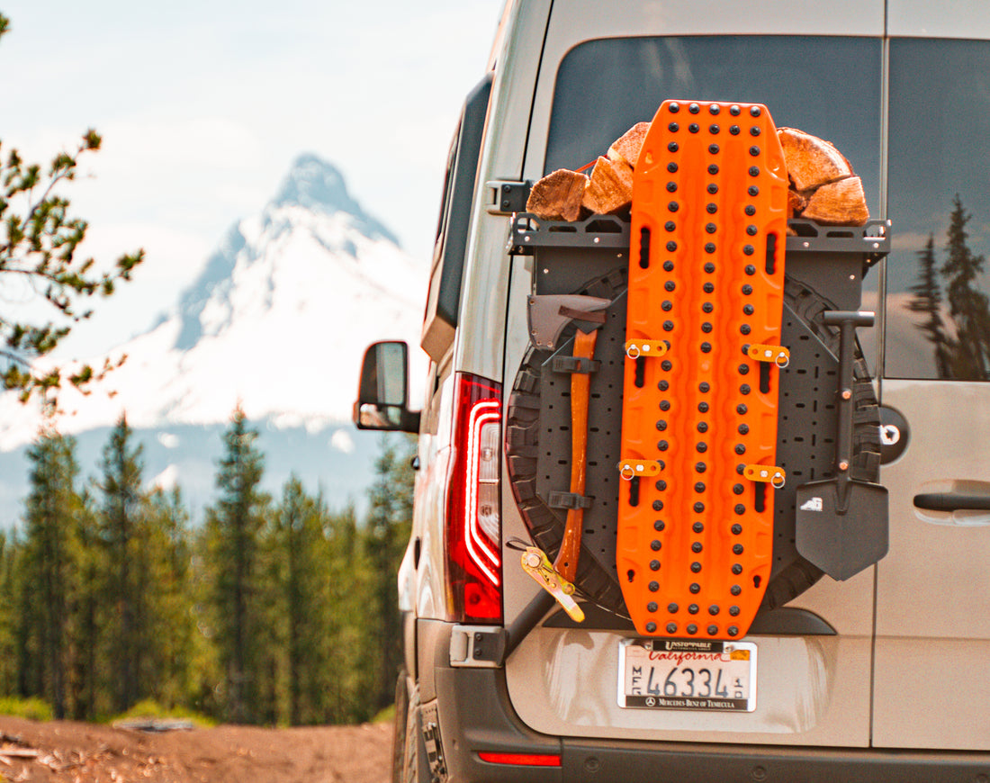 Orange recovery board and firewood mounted on the back of an off-road van with mountain view