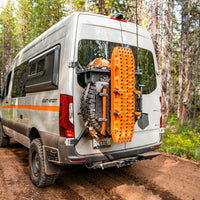 Camper van with off-road recovery gear mounted on rear door parked on forest trail