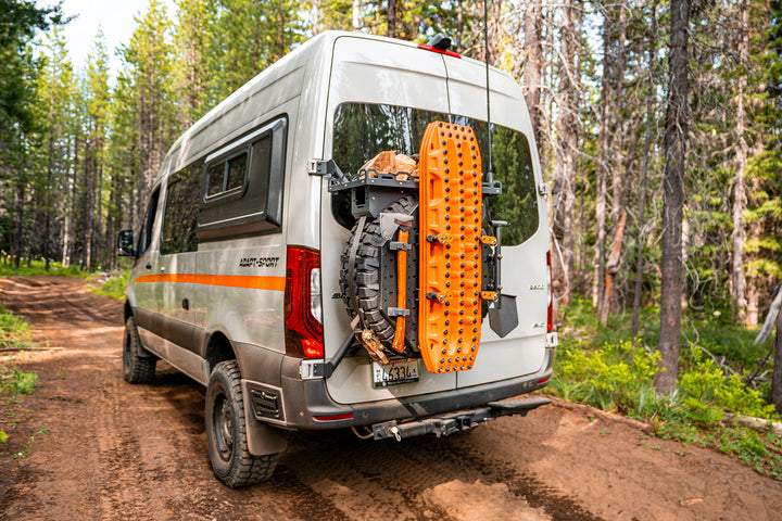 Camper van with off-road recovery gear mounted on rear door parked on forest trail